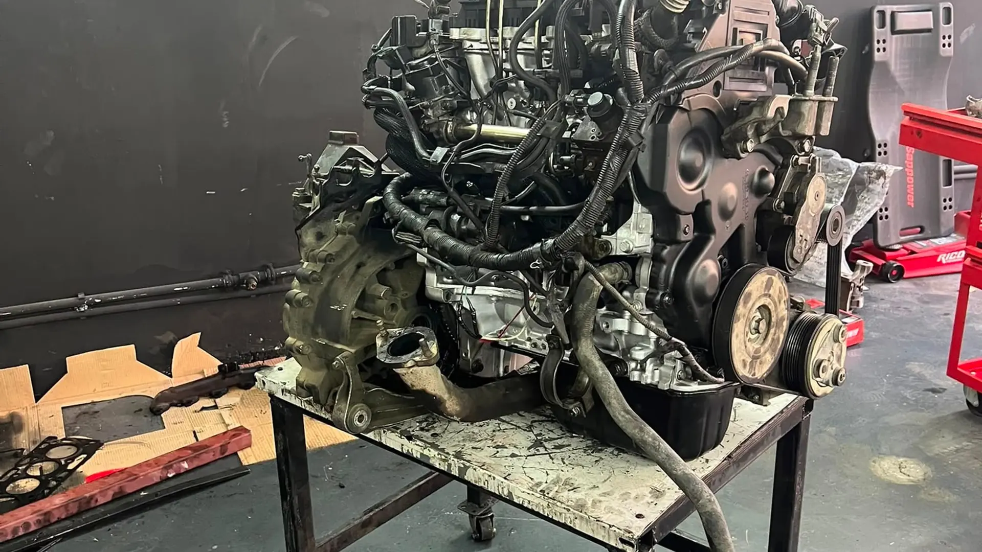 Araçtan sökülmüş motor ve şanzıman grubu, atölye tezgâhının üzerinde